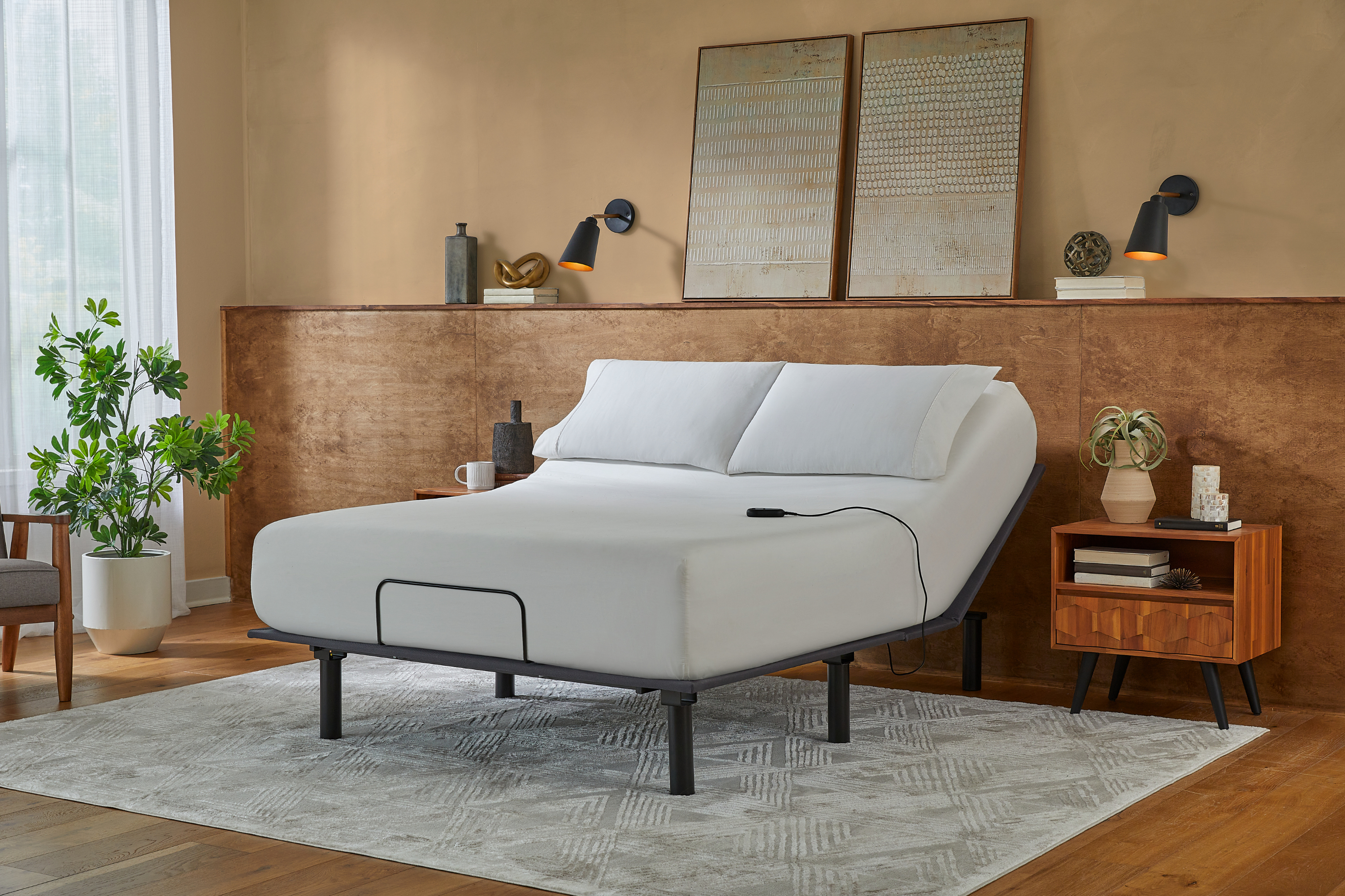 Gray adjustable bed in a bedroom setting with wooden furniture and decor.