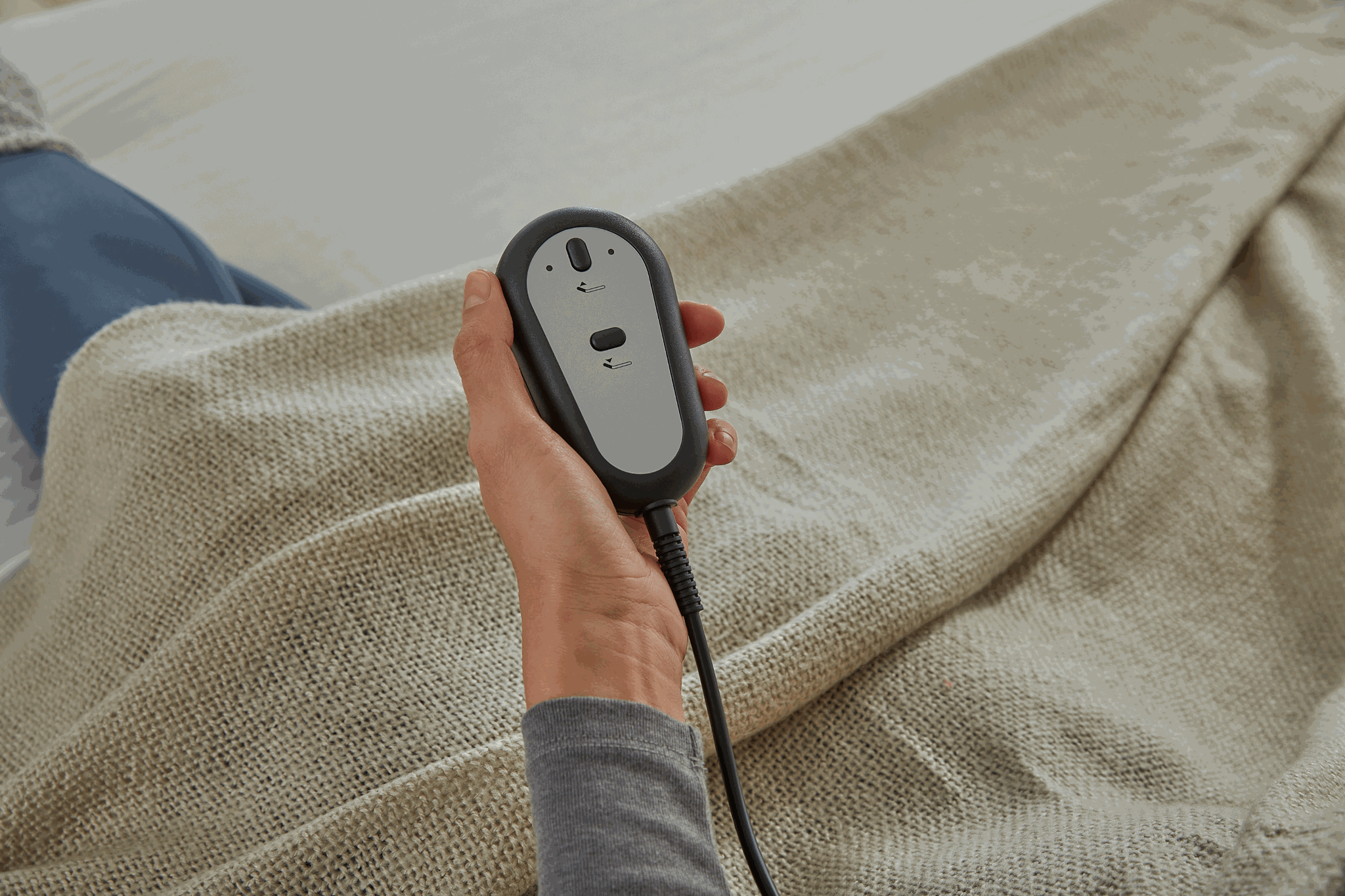 Hand holding a black electronic device with a gray panel over a textured beige fabric background