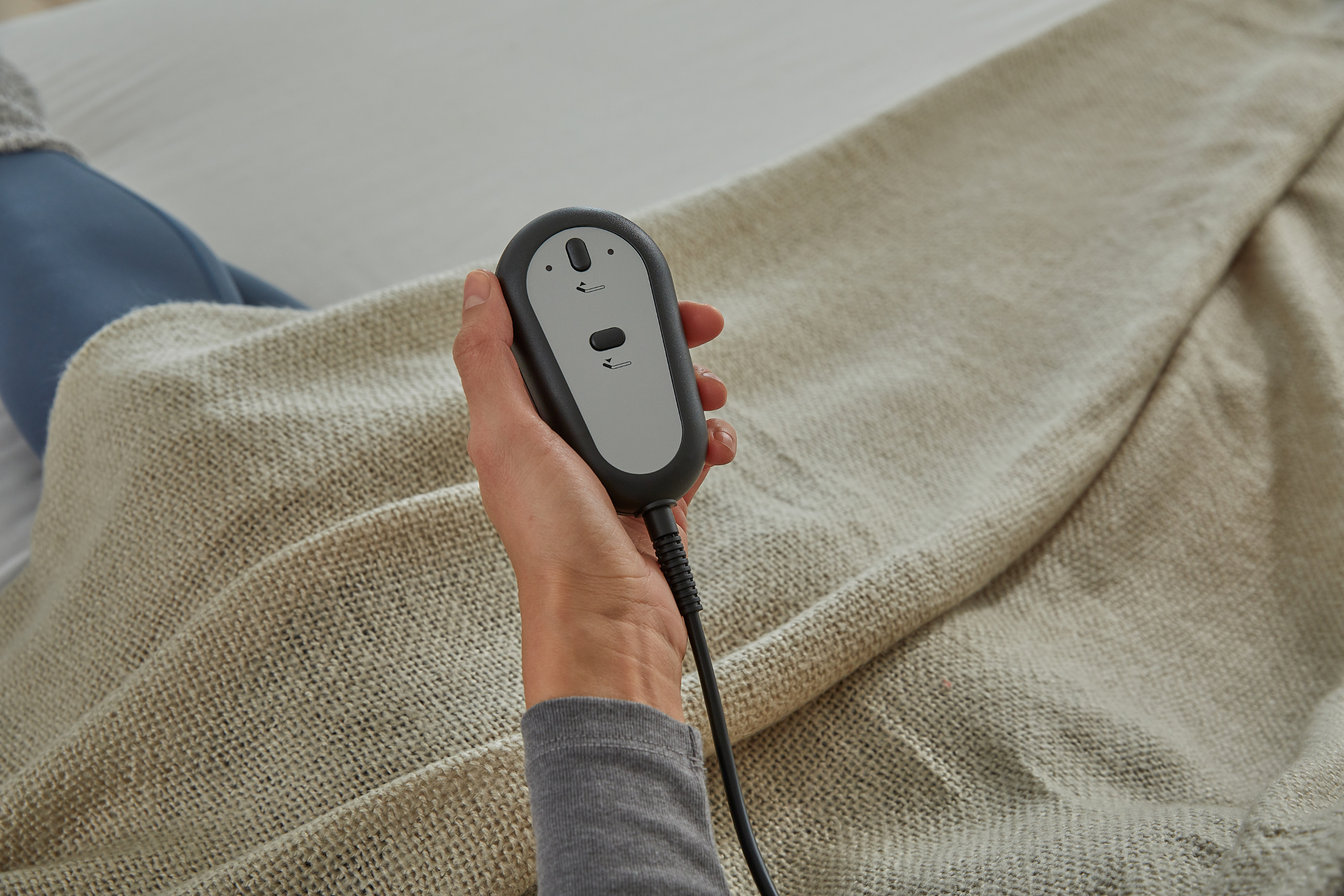 Hand holding a black electronic device with a gray panel over a textured beige fabric background