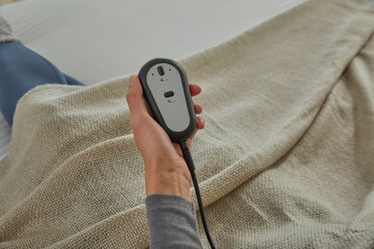 Hand holding a black electronic device with a gray panel over a textured beige fabric background