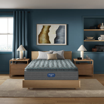 Front room view of Beautyrest Eryx Medium pillow top mattress sitting on wooden bed frame with wooden nightstands wtih blue wall and blue curtains