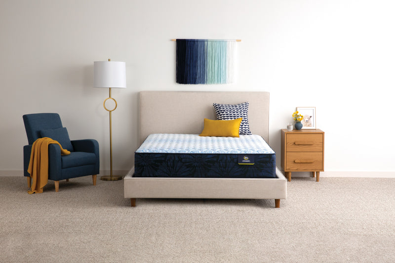 Serta Octave firm tight top mattress in modern room sitting on beige platform with headboard, wooden side table and blue chair with brown throw blanket